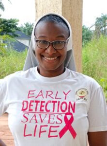 Sr. Akunna showing the theme and the pink ribbon symbol for breast cancer awareness used during school outreach in Nigeria.